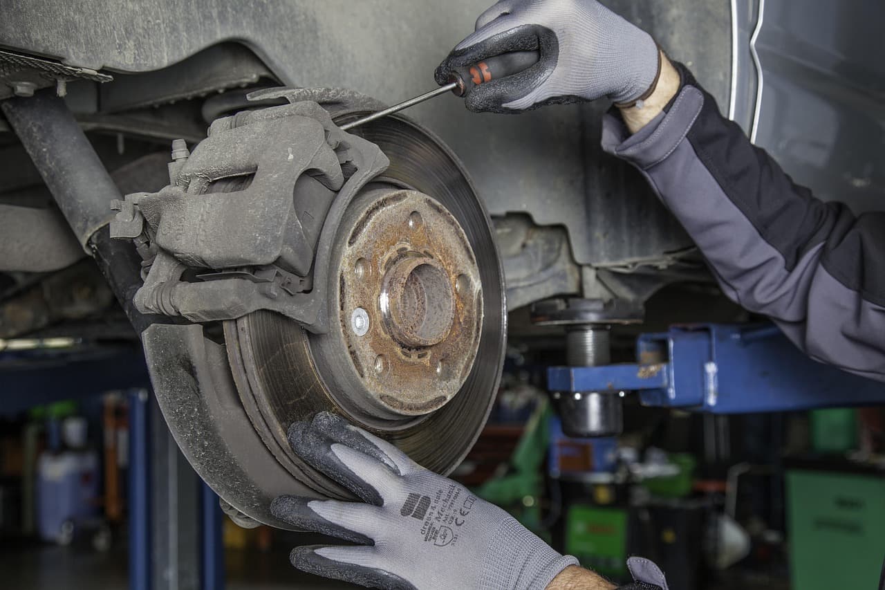 Gloved hands checking a brake disc and caliper on a car on the lift