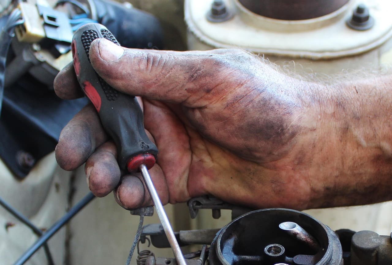 A mechanic's oil-marked hand with a screwdriver, mid-repair